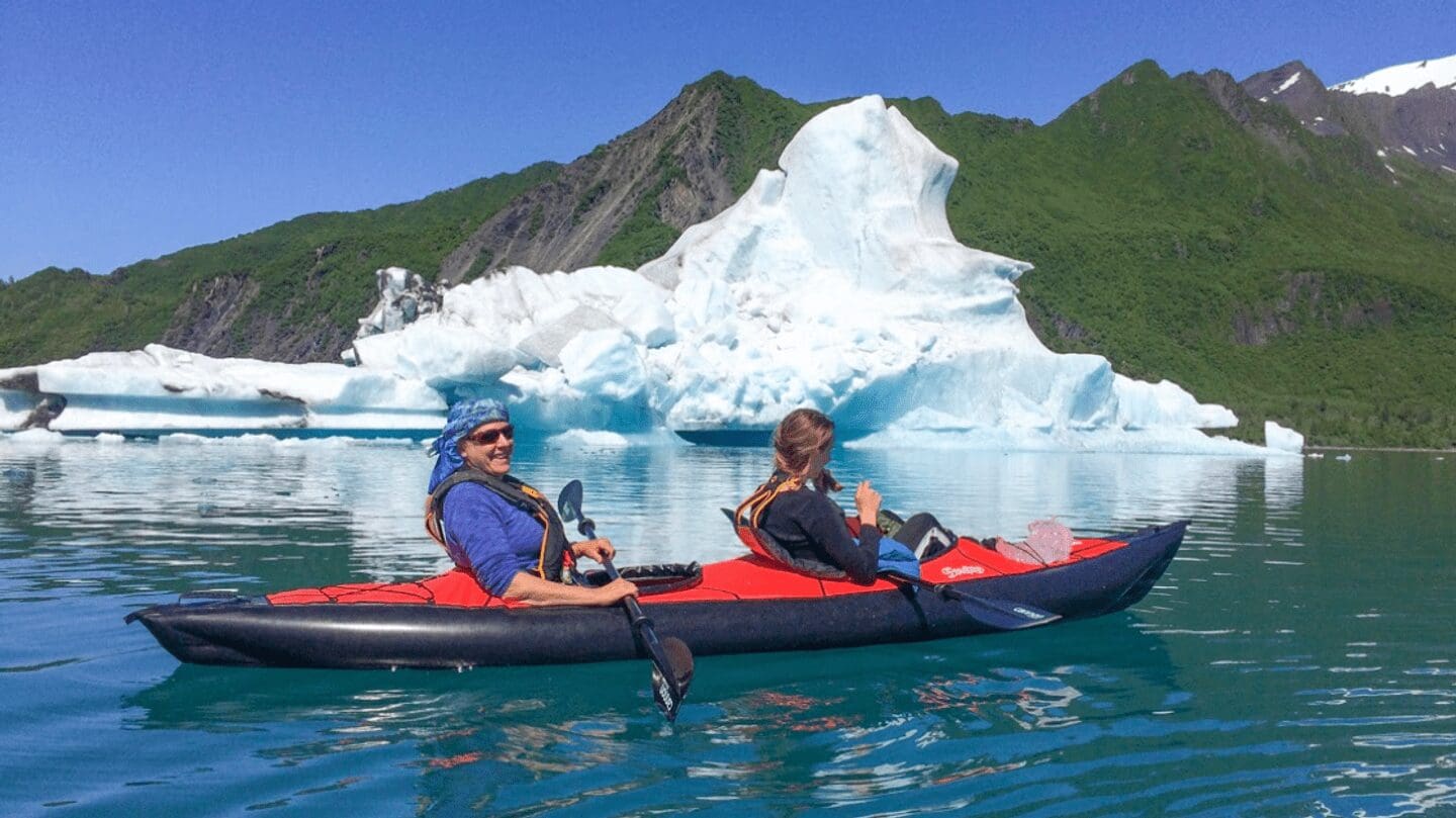 Two people kayaking near a large iceberg.